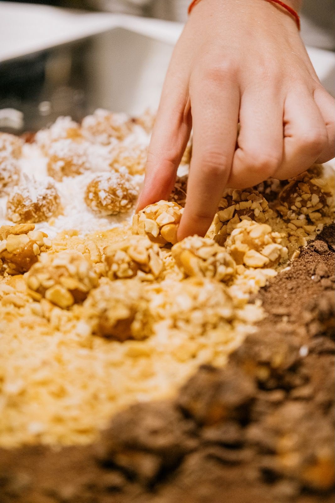 Mão finalizando um brigadeiro empanado em castanhas, no preparo da mesa de doces.
