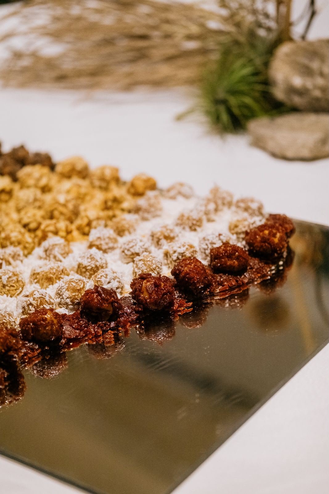 Fileiras de doces cobertos com coco e castanhas sobre travessa espelhada.