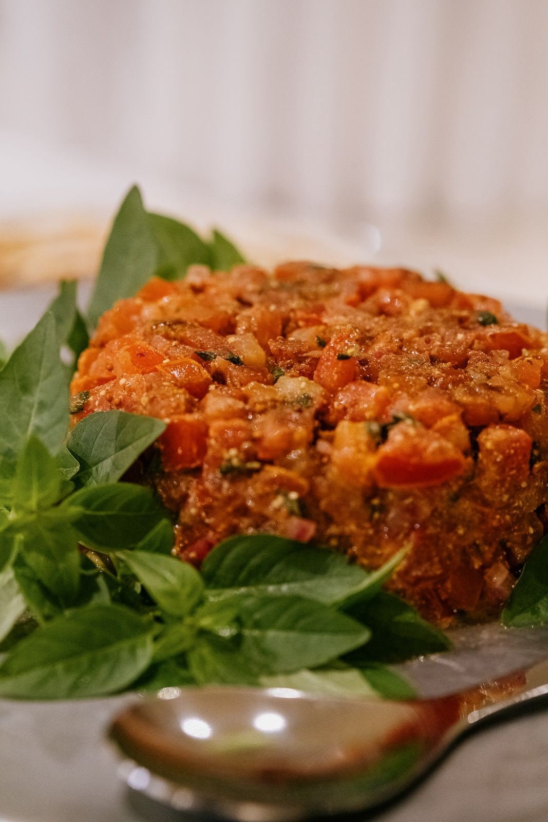 Tartare de tomate finalizado sobre folhas de manjericão fresco, em travessa de prata.